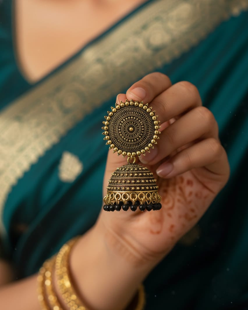 Hand holding a decorative gold ring with a blue saree in the background