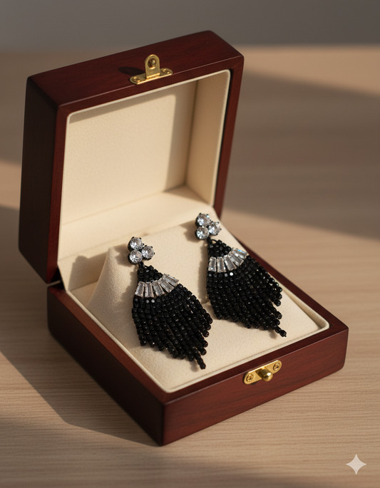 Black beaded earrings in a wooden jewelry box on a wooden surface