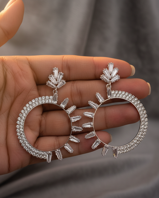 Silver hoop earrings held in a hand against a neutral background