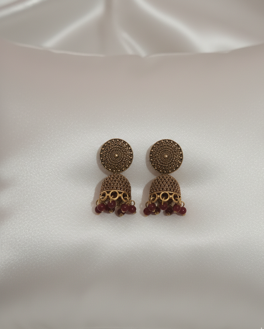 Pair of gold and red earrings on a white satin background