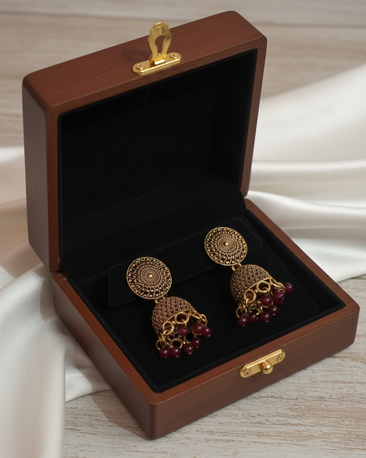 Gold earrings with red stones in a wooden jewelry box on a light background