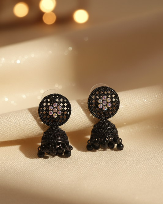 Black earrings with intricate designs on a beige fabric background