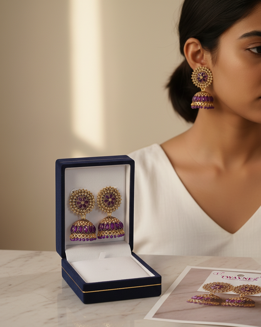 Woman wearing gold and purple earrings with a matching box on a marble surface.