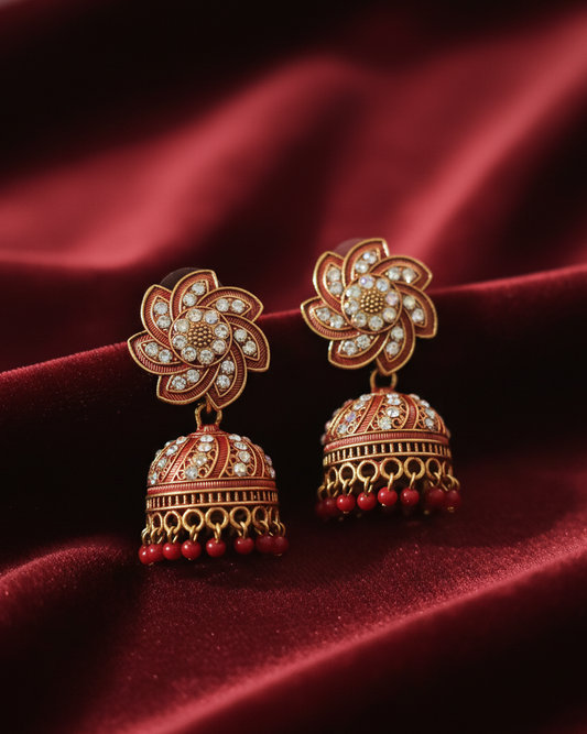 Ornate gold earrings with red beads on a red satin background