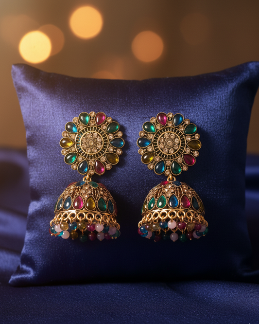 Pair of ornate earrings with colorful gemstones on a blue pillow.