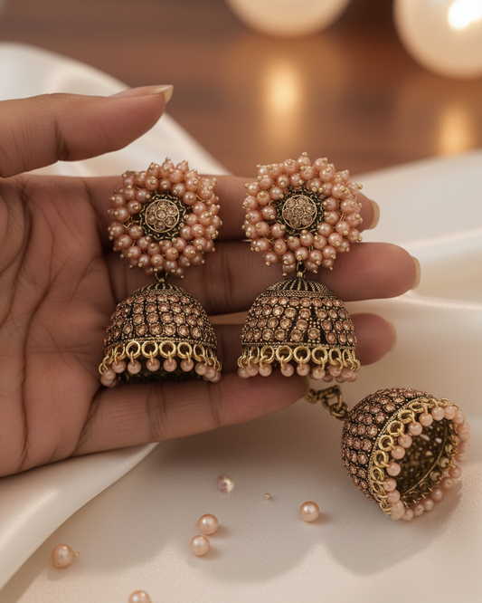 Ornate earrings with pearls held in a hand on a blurred background