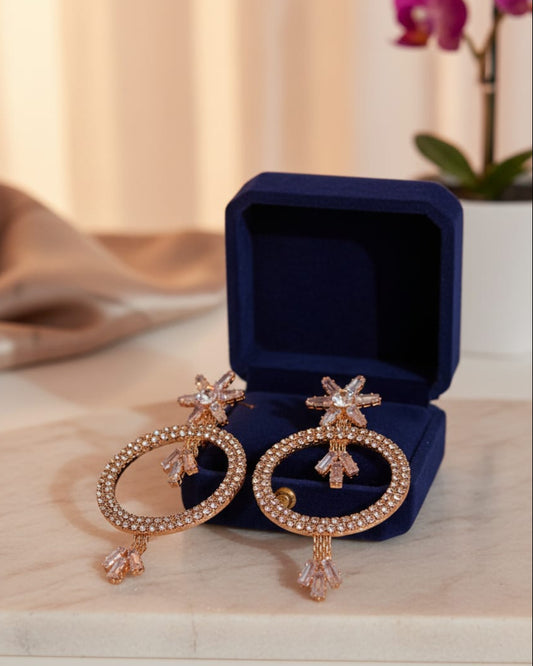 Rose gold earrings with star designs in a blue jewelry box on a wooden surface.